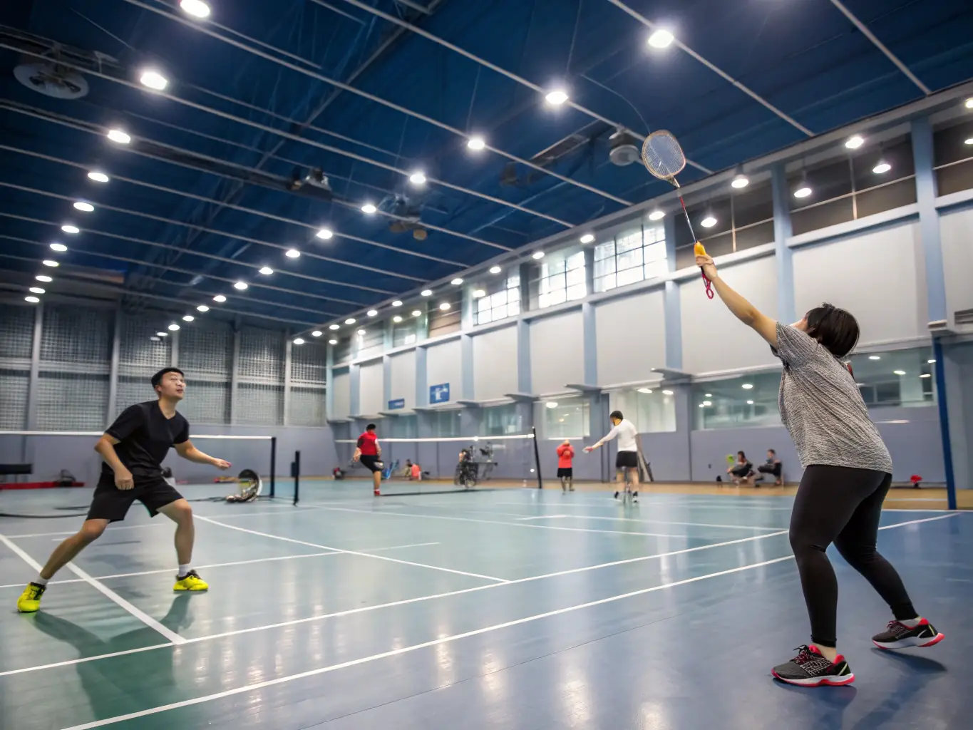 Photo d’une grande salle polyvalente accueillant un tournoi de badminton intergénérationnel, avec des familles et des seniors jouant ensemble, illustrant la diversité des activités proposées.
